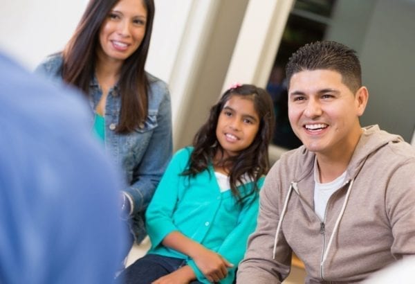 Image of a mother and father sitting down with their young daughter inbetween them.