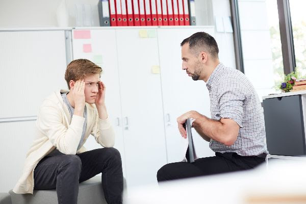 Image of a teenage boy sitting in front of a doctor looking frusterated.