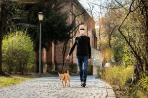 Image of a man wearing a mask while walking his dog outside.