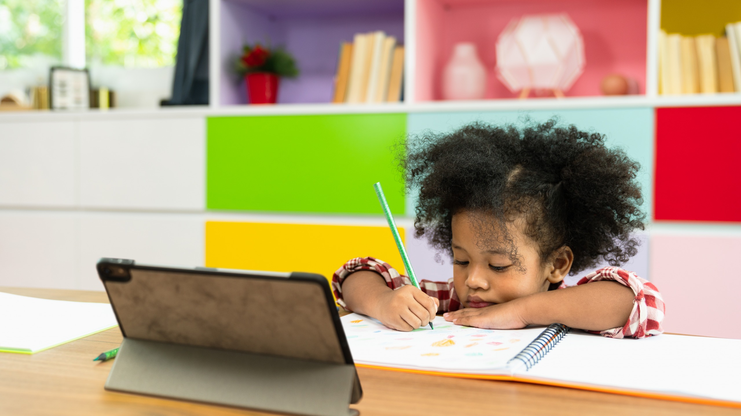 Image of a little girl sitting down in front of a ipad coloring a picture.
