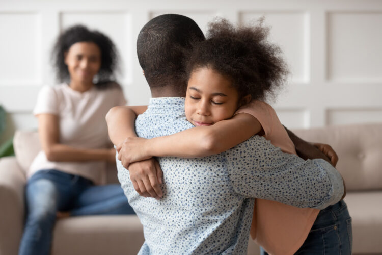 A young girl embraces her father as her mother looks on showcasing effective family communication techniques.