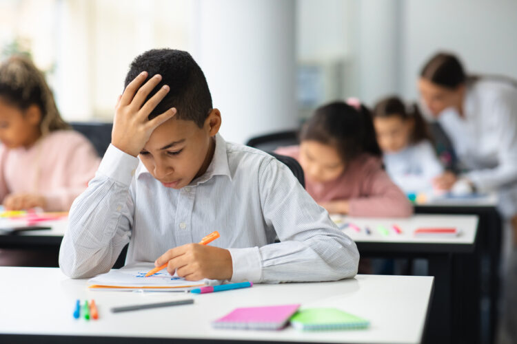 Portrait of boy sitting at desk in classroom and writing